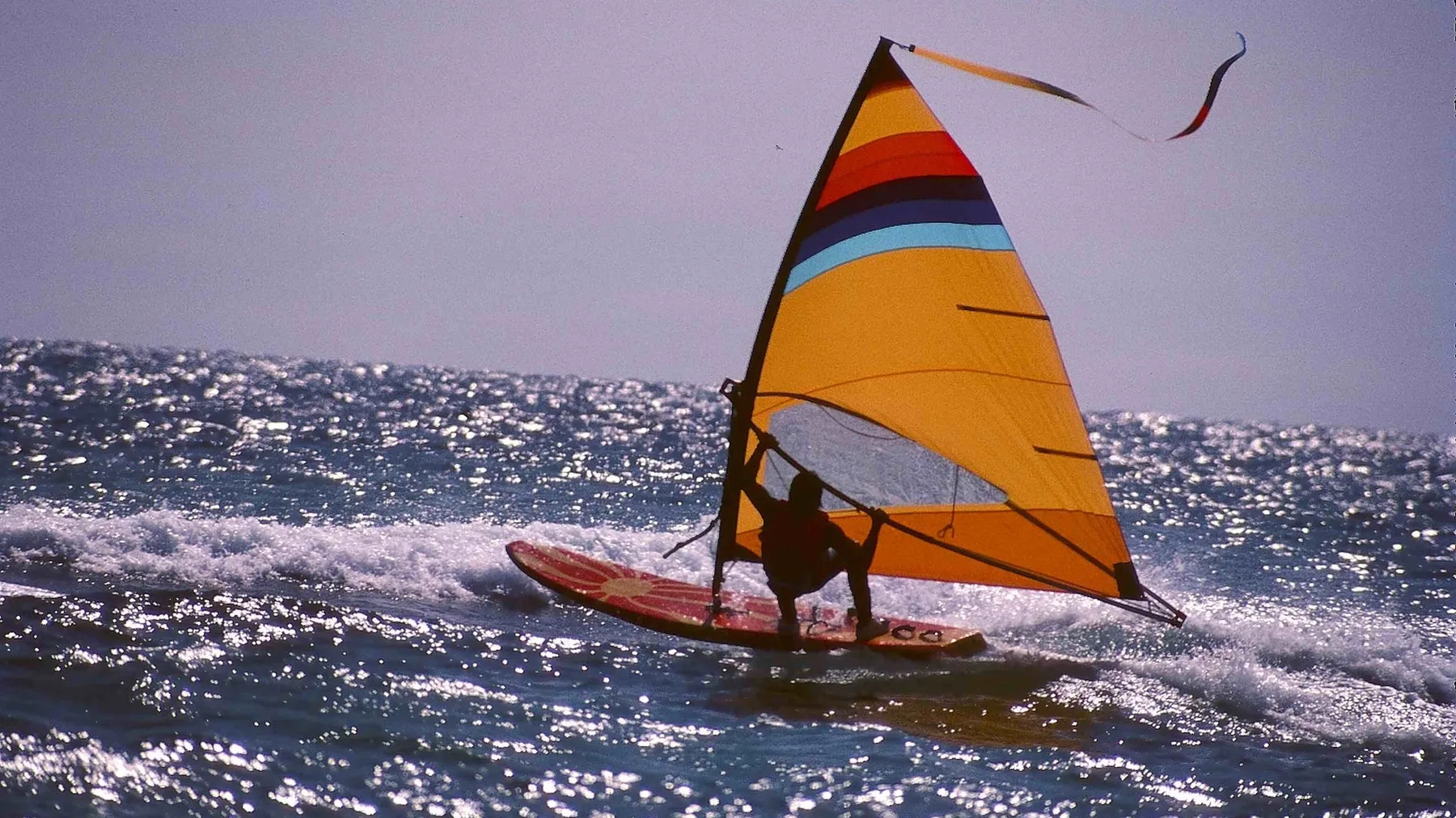 Windsurfer met oranje zeil op glinsterend water
