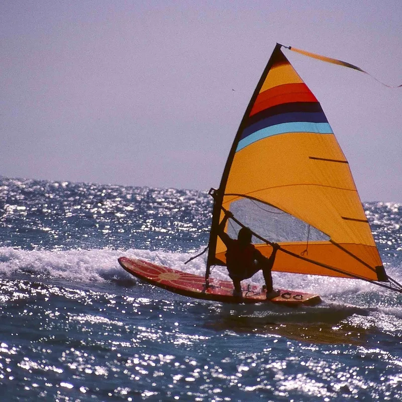 Oude windsurfplank met oranje zeil in de golven