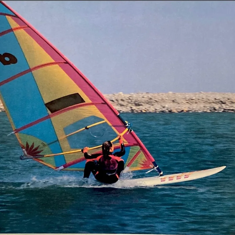 Vintage windsurfplank met roze en geel zeil langs de kust